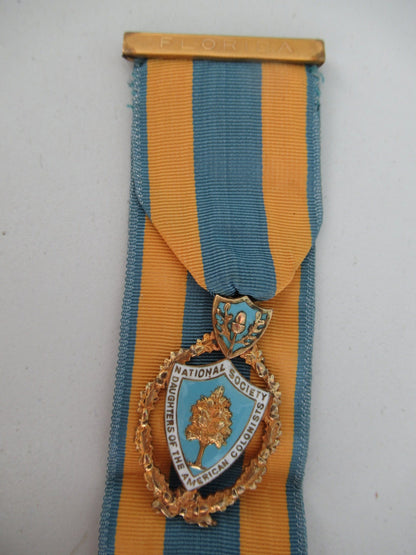 USA SOCIETY BADGE MEDAL FOR THE DAUGHTERS OF THE AMERICAN COLONIALISTS. GOLD FILLED. COMES WITH 7 NAMED RIBBON BARS AND A 'FLORIDA' TOP BAR. NAMED. NUMBERED, AND MARKED. RR!